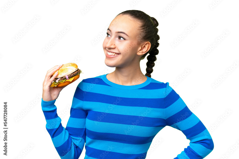 Young Arab woman holding a burger over isolated background posing with arms at hip and smiling Young Arab woman holding a burger over isolated background posing with arms at hip and smiling