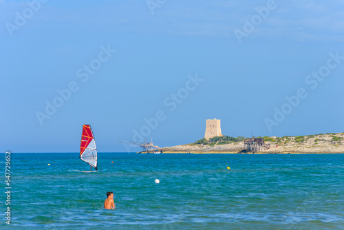 Vieste, Italy. Windsurfer near the Scialmarino beach. The trabucco of Tufara Bay and the Porticello Tower on the background. Summer day along the coast of Vieste. September 7, 2022 photo