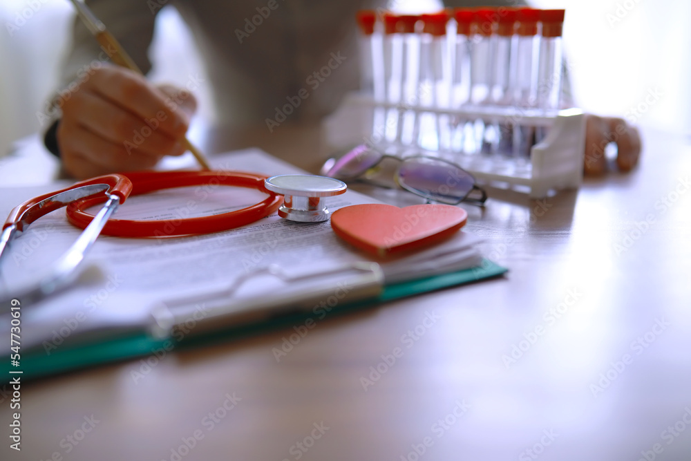 Doctor at his desk in the clinic's office. Stethoscope, test tubes, laptop, prescriptions, glasses on the table.