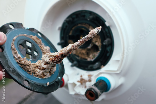 Water heater repair. Repair and maintenance of boilers. The master plumber pulls out a tubular electric heater covered with lime scale from the hole in the boiler.