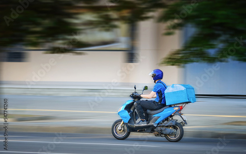 Food delivery moto scooter driver is on his way to deliver food. Courier on motor scooter delivering food. Delivery man in helmet, face mask, gloves ride scooter. Express food delivery, shop online