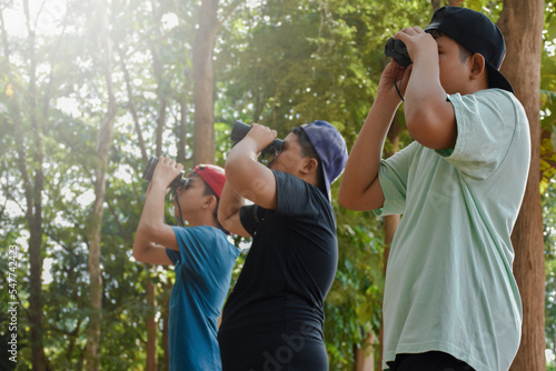 Three Southeast Asian boys are using binoculars to observe birds in tropical forest, idea for learning creatures and wildlife animals outside the classroom.