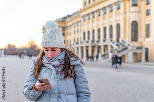 Woman checking news and text on her cellphone outdoor during cold winter season.
