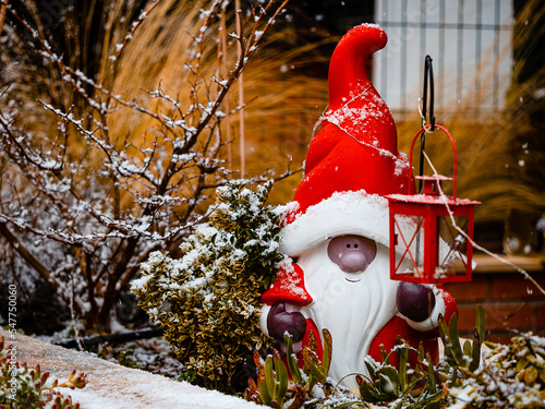 ceramic figurine of st. klaus, in the garden of a house, with snow on the plants and copy space 