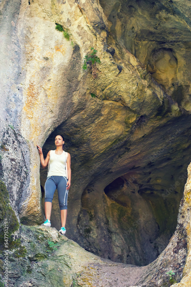 Young woman standing at the cave entrance in summer