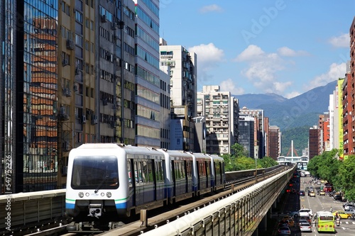 View of a train traveling on elevated rails of Wenhu Line in Taipei Metro System by office towers under blue clear sky ~View of MRT railways in Taipei, capital city of Taiwan, on a beautiful sunny day