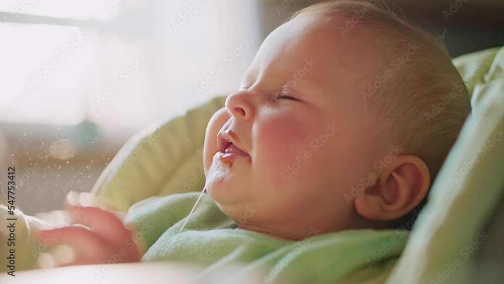 Close up face of child sneezing and looking to sides sitting in the feeding chair. Mom trying to feed the kid. Sunlight. Smiling. Funny. Slow motion Close up face of child sneezing and looking to sides sitting in the feeding chair. Mom trying to feed the kid. Sunlight. Smiling. Funny. Slow motion