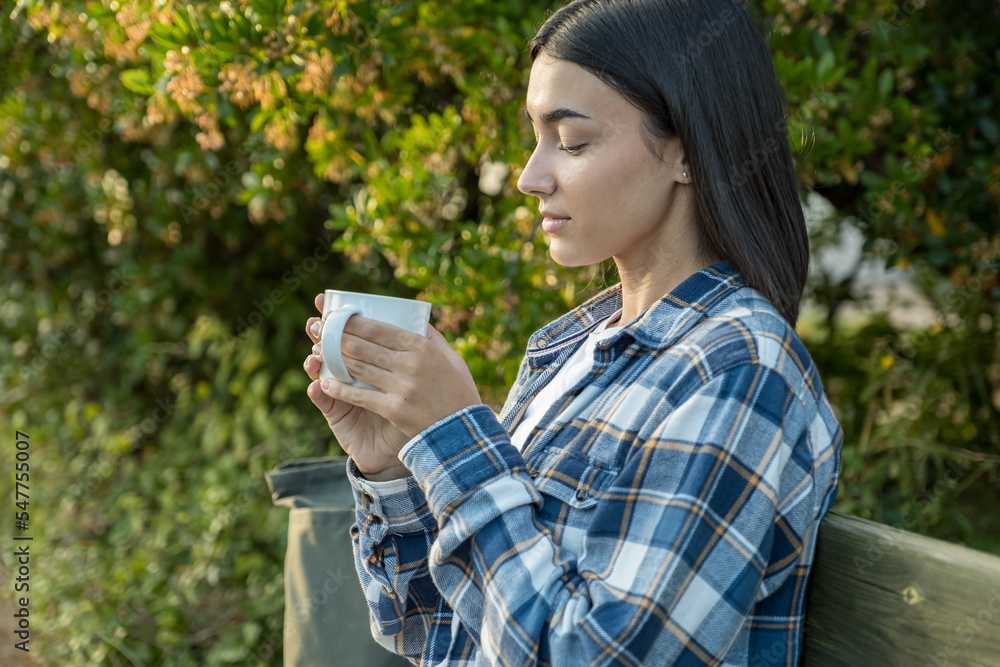 Girl sitting on a bench drinking coffee with trees in the background Girl sitting on a bench drinking coffee with trees in the background