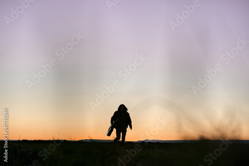 silhouette of a caucasian boy with long hair holding a guitar running towards camera at sunset