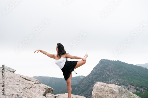 caucasian mature woman in white top and black skirt doing ballet exercises on a big rock in the mountains