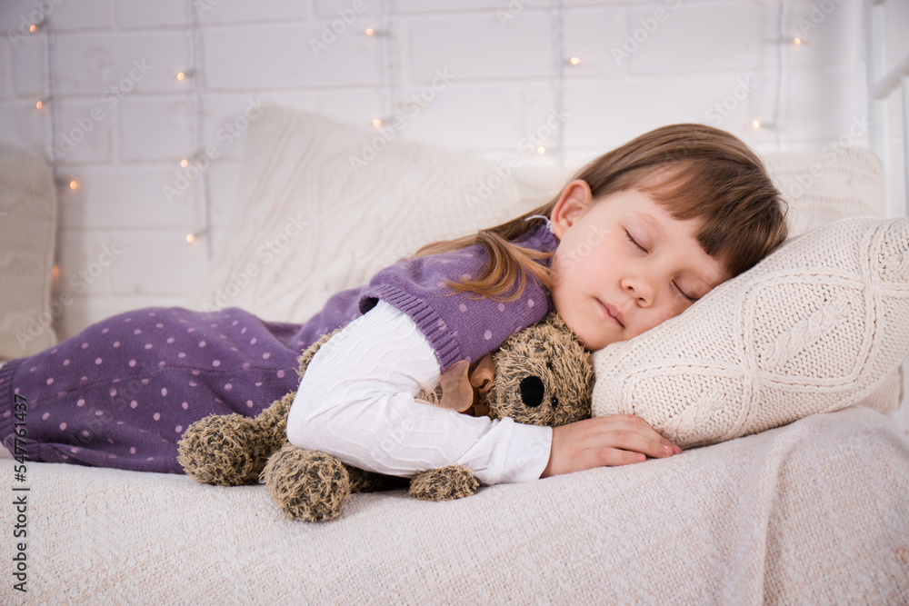 A girl with a teddy bear is sleeping on a cozy bed A girl with a teddy bear is sleeping on a cozy bed