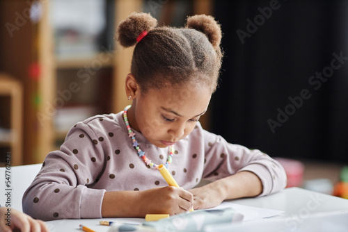 Photos Cute serious African American schoolgirl drawing with yellow highlighter while s