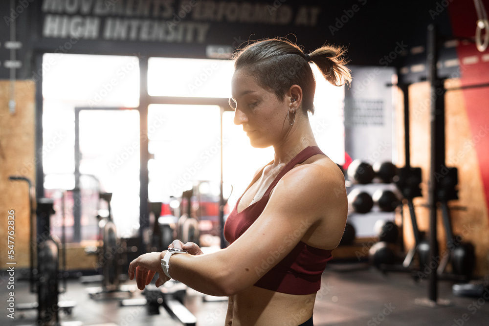 Caucasian young woman doing sports in a gym looking at the watch on her left arm Caucasian young woman doing sports in a gym looking at the watch on her left arm