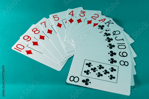 A fan of white cards of diamonds and cross suits, red and black, respectively, on a turquoise background.