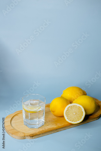 yellow lemons lie on a wooden board with a glass of water on a blue background