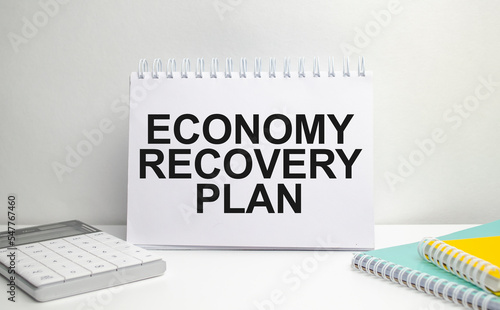 ECONOMY RECOVERY PLAN words on paper notebook with office supplies