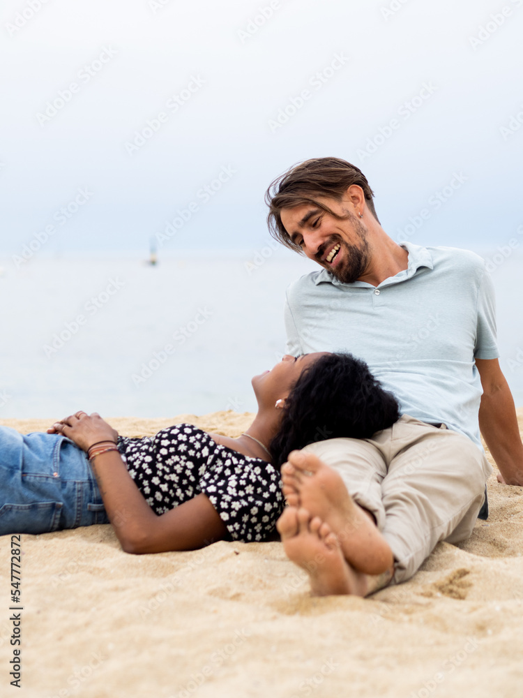 Heterosexual diverse young couple sitting affectionately in front of the sea 