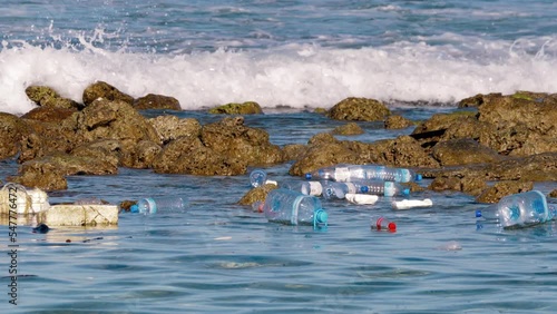 Empty plastic bottles and other rubbish float in sea between the stones near the seashore. Ecology of the earth, seas and oceans is in danger due to the large amount of garbage of human civilization photo