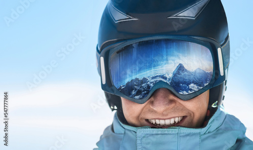  Man on the background blue sky. Wearing ski glasses. Winter Sports. A mountain range reflected in the ski mask.