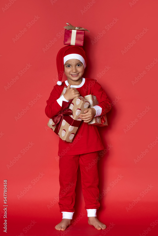 Cute baby boy in Christmas pajama with presents on red background.