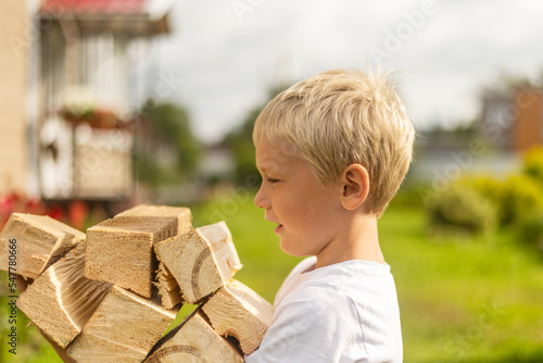 portrait of a boy with blond hair carrying an armful of firewood into the house
