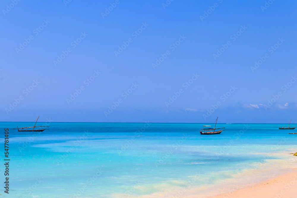 View of tropical sandy Nungwi beach and traditional wooden dhow boats in the Indian ocean on Zanzibar, Tanzania View of tropical sandy Nungwi beach and traditional wooden dhow boats in the Indian ocean on Zanzibar, Tanzania