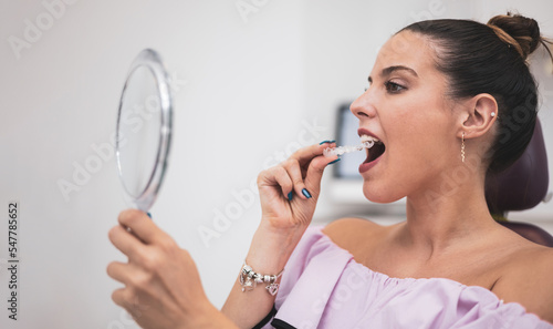 A pretty woman puts on dental splints using a mirror in a dentist clinic. Bruxism concept, perfect bite. Side view.