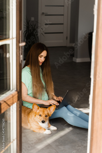 Pregnant girl with laptop and Corgi dog sitting on the floor and chatting online with friends. Lifestyle pregnancy with Welsh Corgi Pembroke.