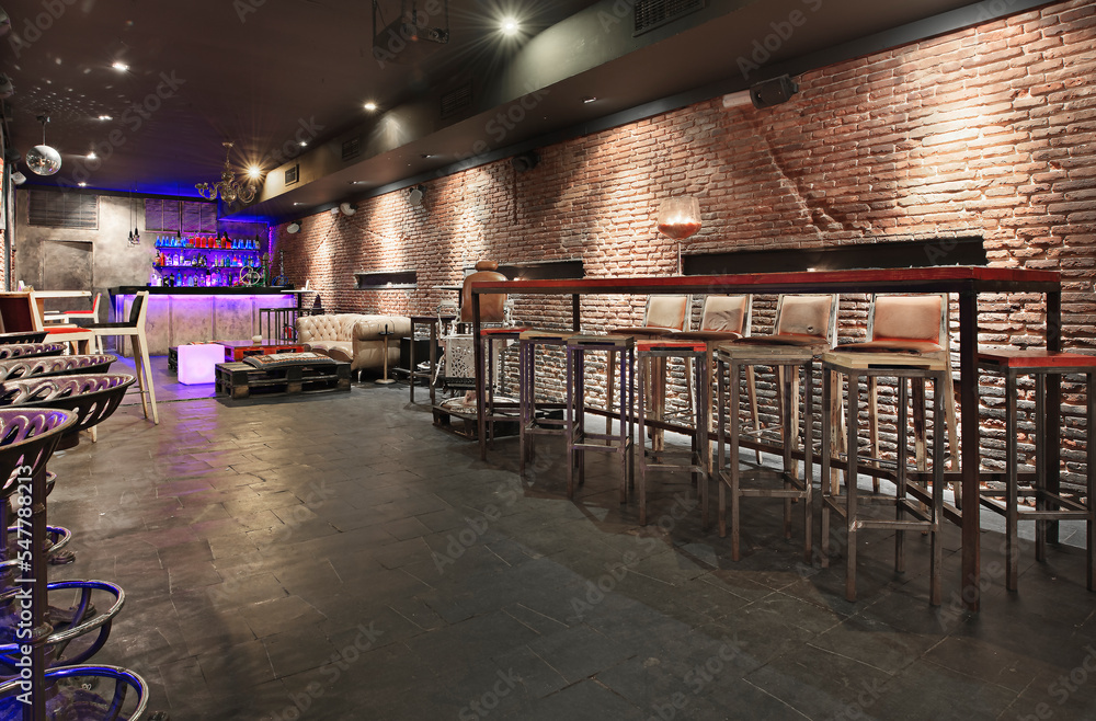 Living room of a nightclub with exposed brick walls, high wooden and metal tables and matching high stools