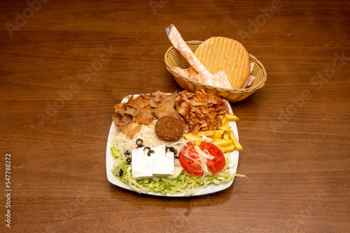 Typical kebab platter with falafel, onion, white rice, lamb meat and lettuce along with a portion of French fries on a white plate and bread with cutlery in a basket