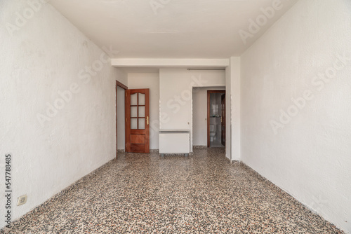 Empty room with old polished terrazzo floors and reddish wooden doors with a gray electric heat accumulator