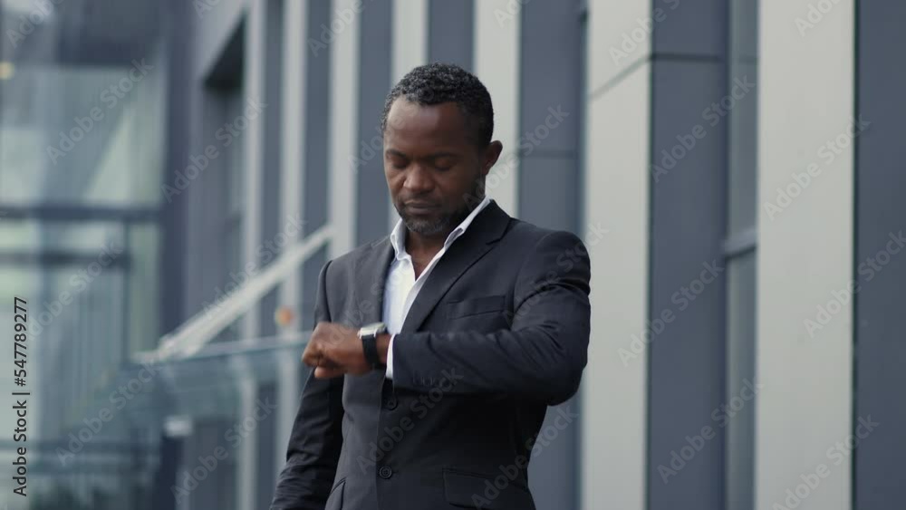 Time for break. Middle aged african american businessman looking at watch and drinking coffee outdoors, slow motion Time for break. Middle aged african american businessman looking at watch and drinking coffee outdoors, slow motion