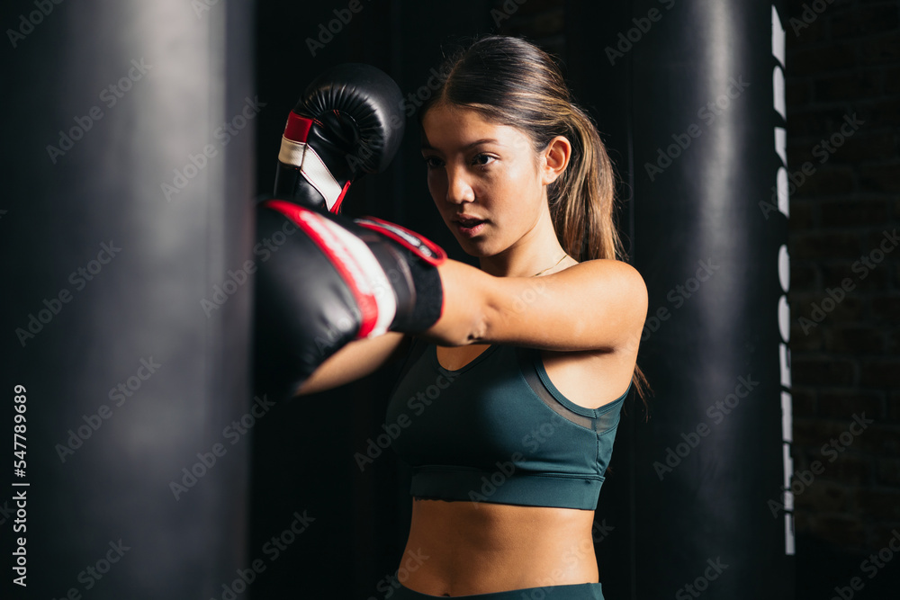 Women's boxing, physical exercise of a girl in a boxing class, the woman hits the punching bag with a glove. Youth sports concept.