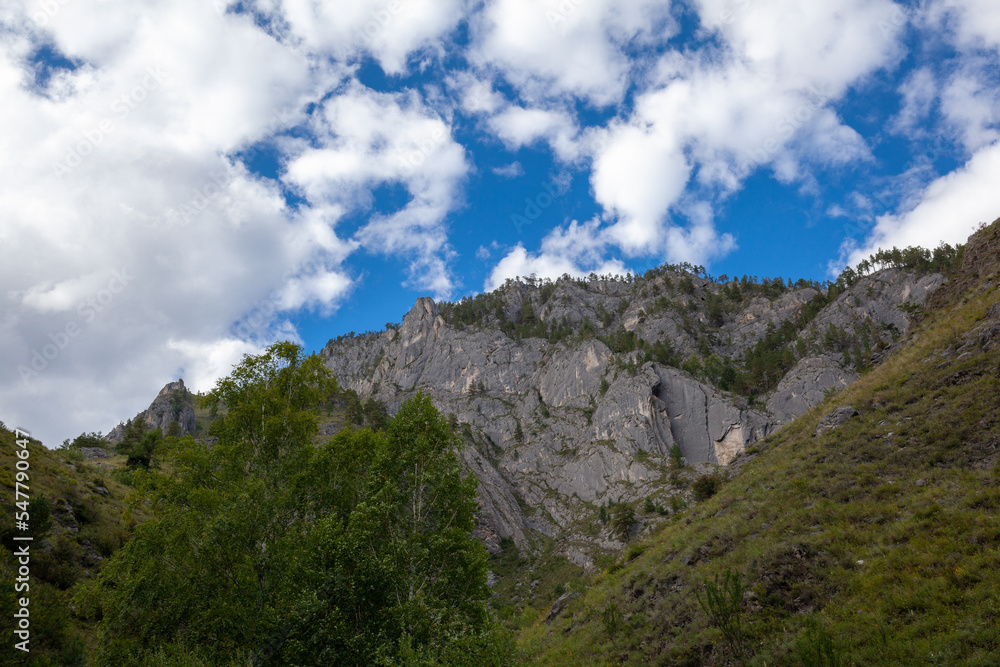 A large mountain with a sheer cliff close-up against the sky. Hiking tourism. Mountains of the Altai Mountains, Altai Republic A large mountain with a sheer cliff close-up against the sky. Hiking tourism. Mountains of the Altai Mountains, Altai Republic