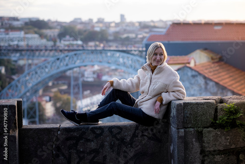 A female tourist sits on a masonry wall in Porto, Portugal..