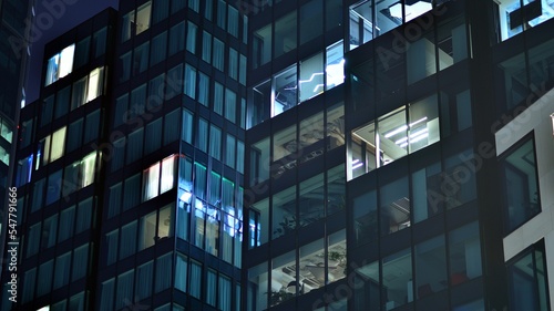 Modern office building in city at the night. View on illuminated offices of a corporate building. Blinking light in window of the multi-storey building of glass and steel. Long exposure at night