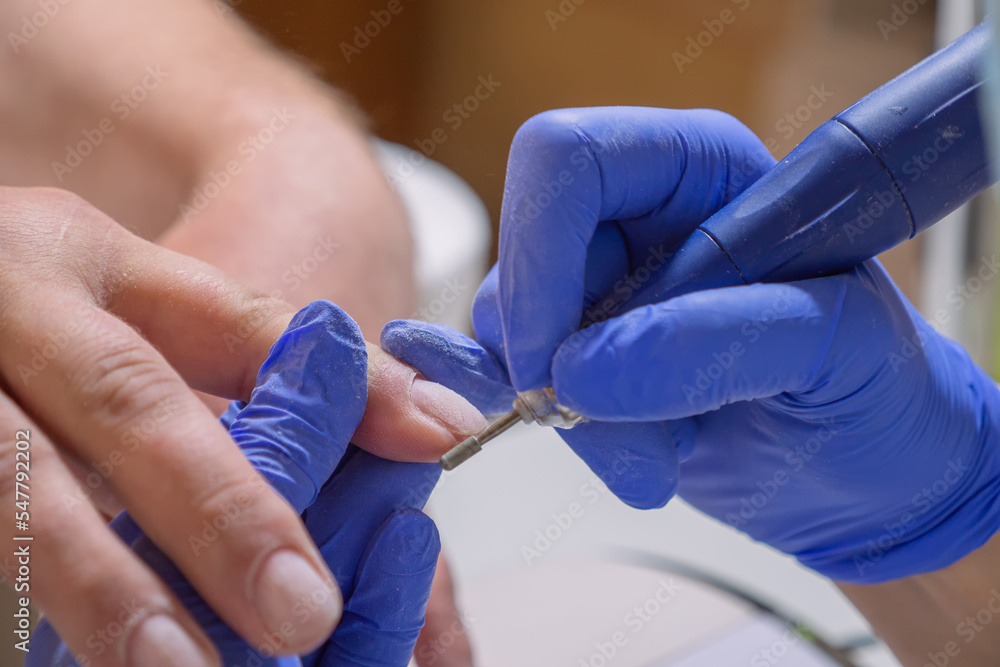 Manicurist master removing cuticles. Processing of rough cuticles and lateral folds of male nails on hands with a conical instrument. Medical hardware manicure in a beauty salon Manicurist master removing cuticles. Processing of rough cuticles and lateral folds of male nails on hands with a conical instrument. Medical hardware manicure in a beauty salon