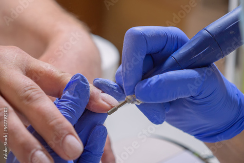 Manicurist master removing cuticles. Processing of rough cuticles and lateral folds of male nails on hands with a conical instrument. Medical hardware manicure in a beauty salon