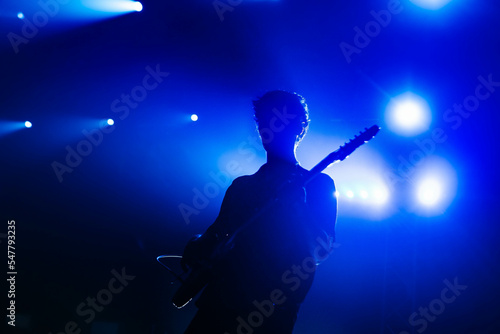 Guitarist plays solo on stage. A band silhouette.