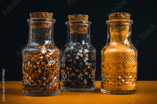 Spices in glass jars. Hot pepper, black pepper and curcuma powder in containers closed with corks.