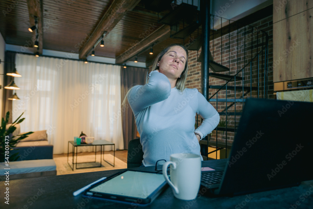 Obraz premium Tired female freelance has neck pain and a headache while working from home with tablet and laptop.