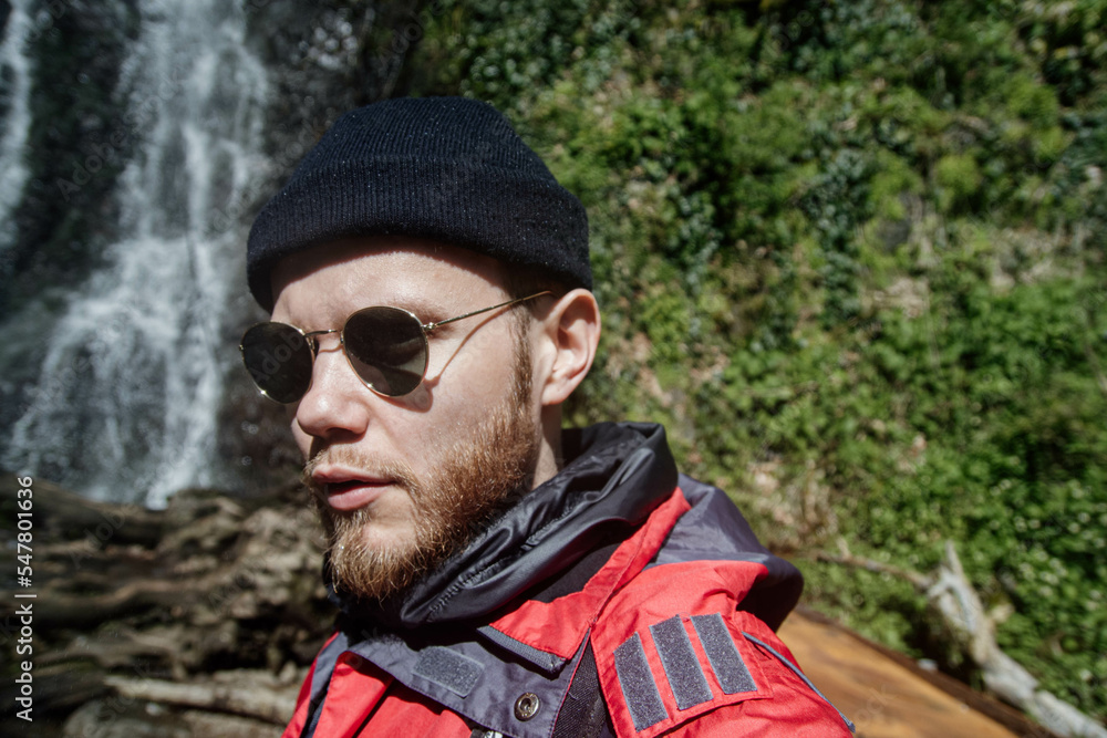 male traveler with a beard on a hike against the backdrop of a waterfall in the mountains male traveler with a beard on a hike against the backdrop of a waterfall in the mountains