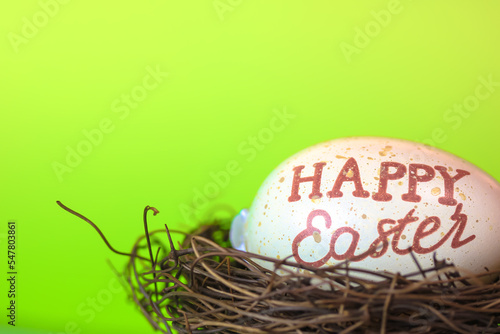 Chicken egg with Happy Easter text in bird's nest isolated on green background.