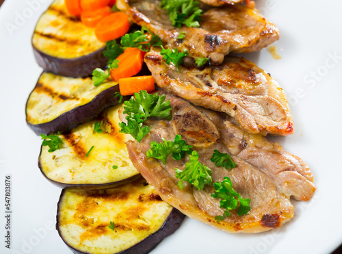 Delicious broiled lamb loin chops served on white plate with grilled eggplant and carrots..