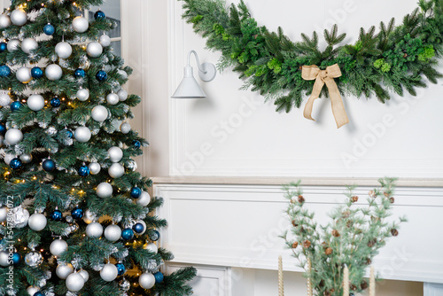 A decor made of Christmas tree branches hangs on the wall near a white sconce. Festive New Year's decor on the wall at home © Дмитрий Ткачук