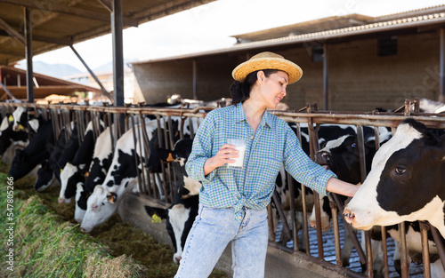 Smiling asian woman professional farmer posing with glass of milk at the cow farm