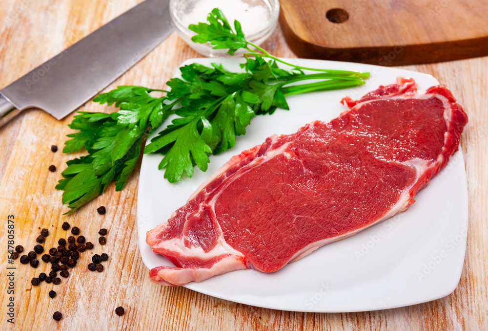 Ingredients for cooking. Raw beef entrecote with fresh parsley and spices on wooden surface