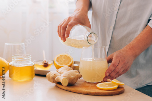Woman pours freshly prepared drink from ginger root lemon honey into glass. Health tea, antioxidant