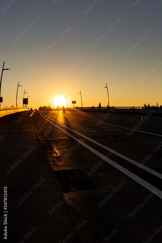 Marathon runners running towards sunrise on a bridge