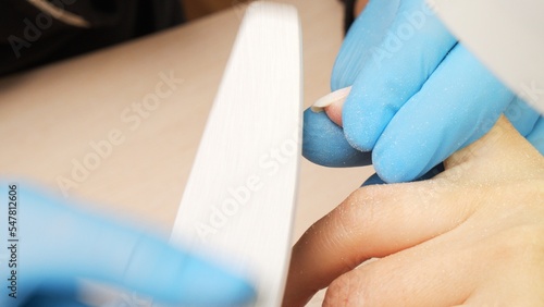 Manicurist files the shape of the nails with a special nail file, close up view. The manicurist shapes the nails with a nail file. The process of nail care in a beauty salon. Nail file processing.